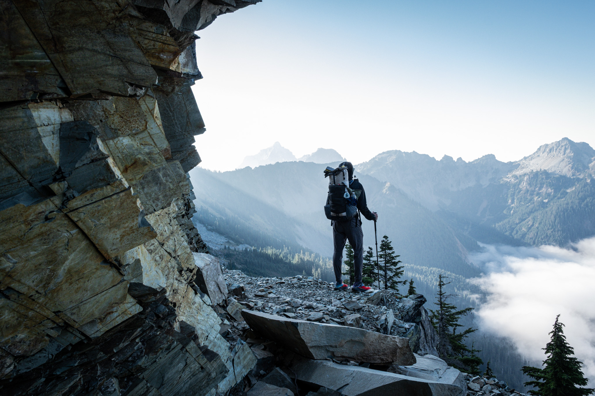 Hiker on a rocky mountain overlook above clouds at sunrise.